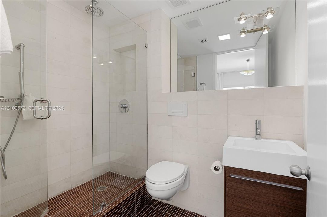 Glass-enclosed walk-in shower with rain showerhead, wall-mounted toilet, floating wood-finish vanity with rectangular vessel sink, and large wall-mounted mirror