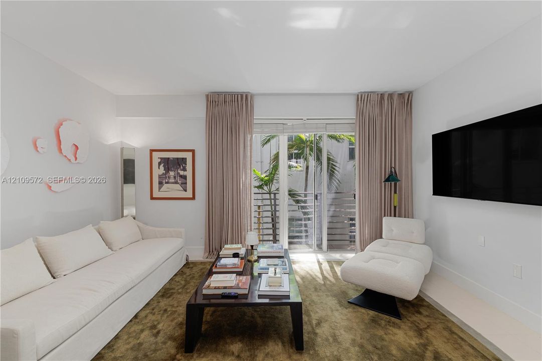 Sliding glass doors leading to a private balcony featuring metal railings and palm tree greenery