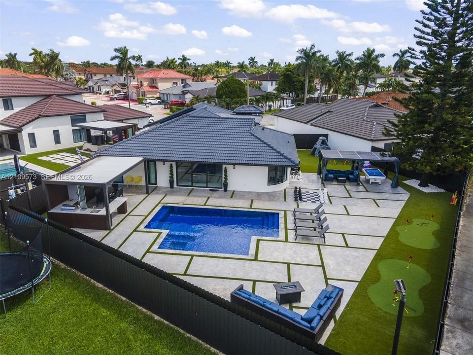 Backyard oasis featuring an in-ground swimming pool, custom hardscaping with integrated turf, a built-in outdoor kitchen, and a dedicated putting green