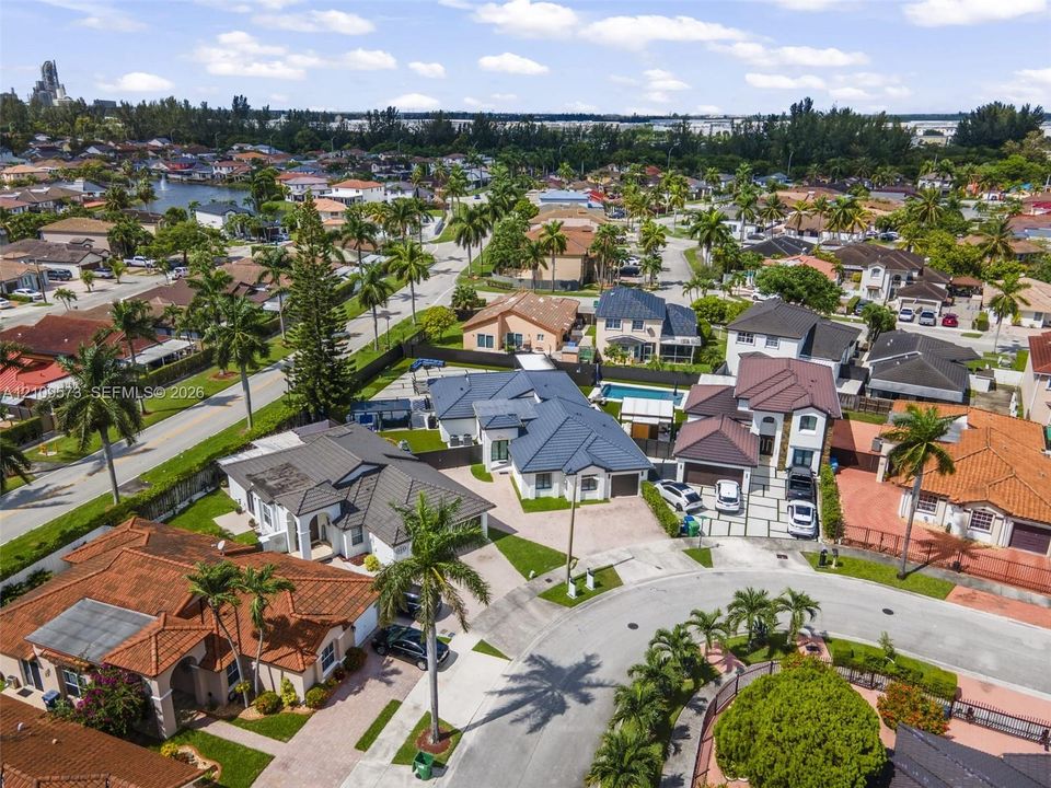 Aerial perspective of a residential neighborhood featuring paved streets, mature palm trees, diverse architectural styles, and private swimming pools