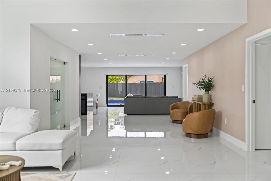 Open floor plan interior featuring polished large-format tile flooring, recessed ceiling lighting, a frosted glass door, and expansive black-framed sliding glass doors
