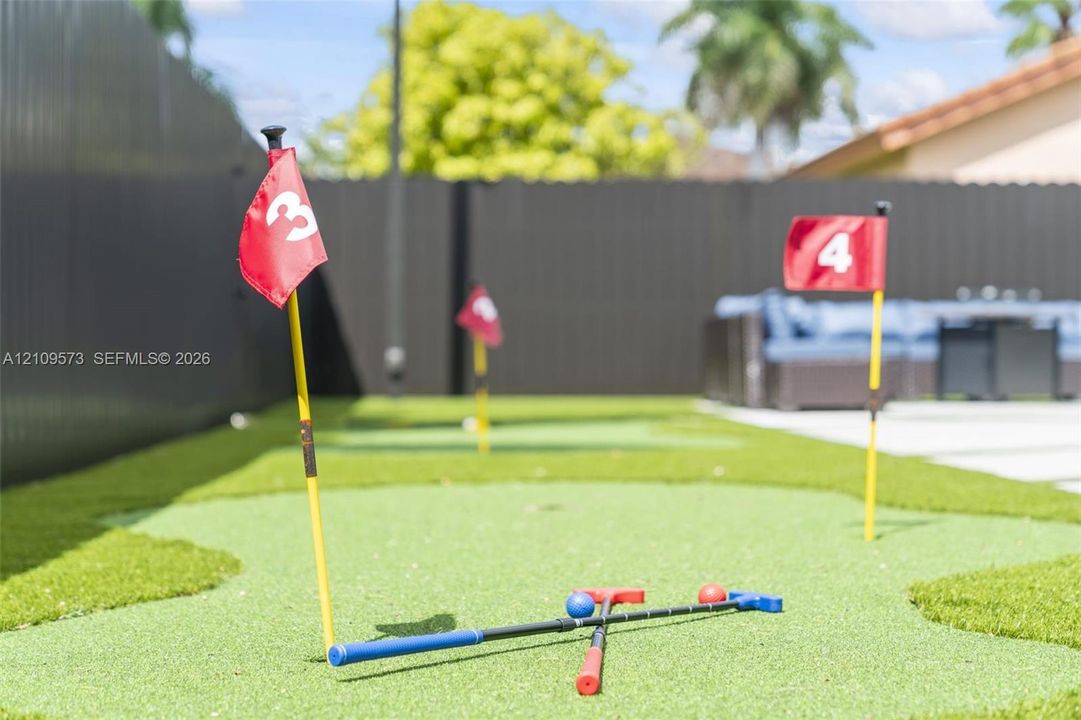 Backyard putting green featuring synthetic turf, numbered hole markers, and privacy fencing