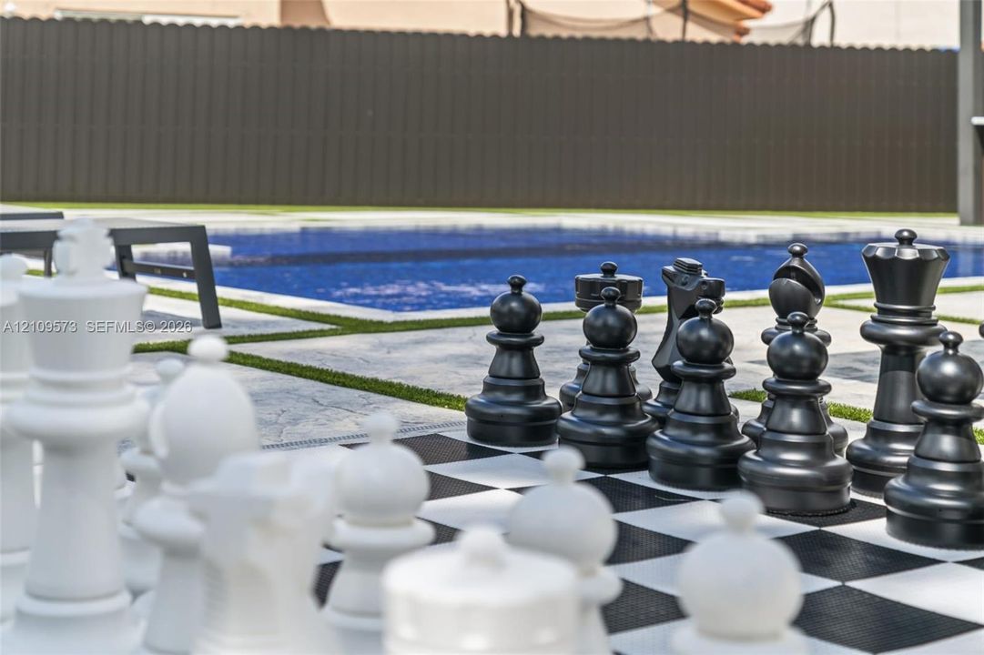 Outdoor recreational area featuring a large-scale chess set, inground swimming pool, concrete hardscaping, and synthetic turf lawn accents