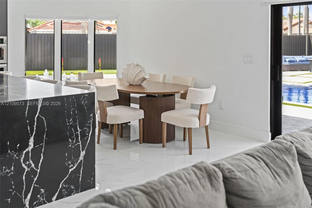 Large-format tile flooring, kitchen island with black-veined stone countertop, and sliding glass doors with exterior pool access