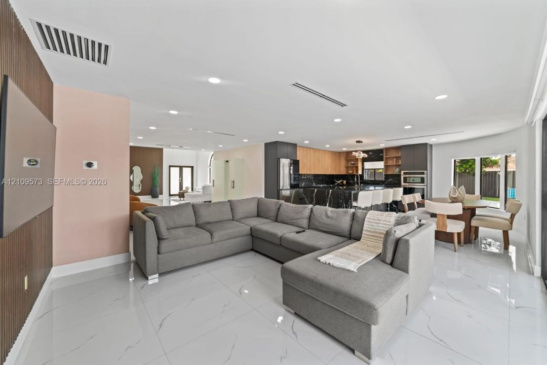 Open-concept interior featuring large-format tile flooring, recessed ceiling lighting, a wood-slat accent wall, and a kitchen equipped with a stone-top island and dark cabinetry