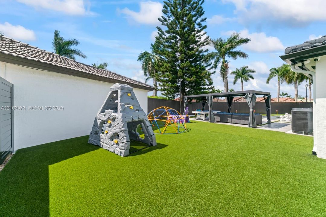Backyard featuring synthetic turf, perimeter privacy fencing, and a metal-framed pergola