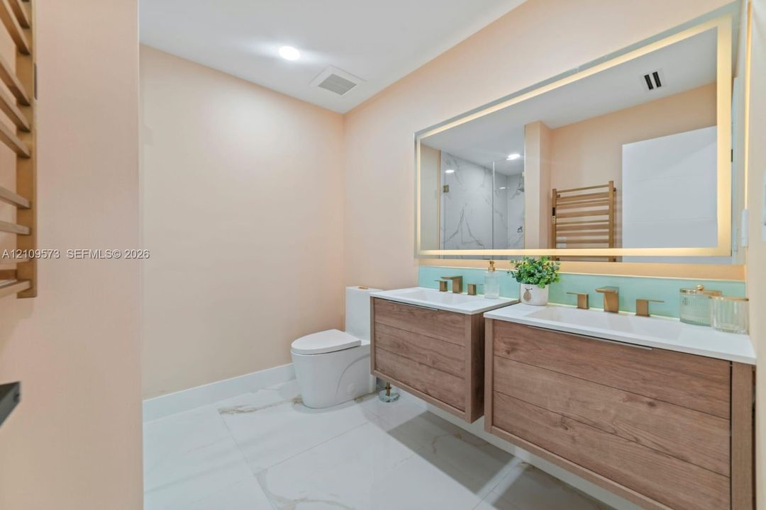 Double floating vanity with wood-finish cabinetry, rectangular vessel sinks, metallic hardware, and a large integrated LED-backlit mirror, complemented by large-format tile flooring