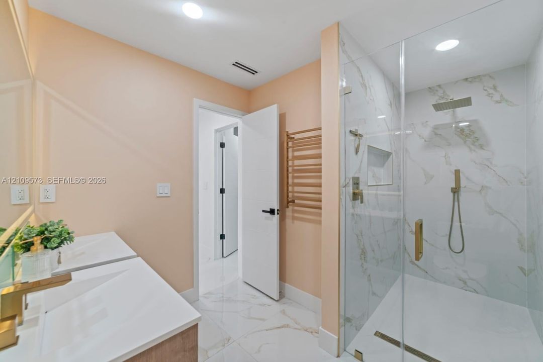 Walk-in shower with floor-to-ceiling stone-patterned tile, rainfall showerhead, wall-mounted hand sprayer, and built-in recessed niche