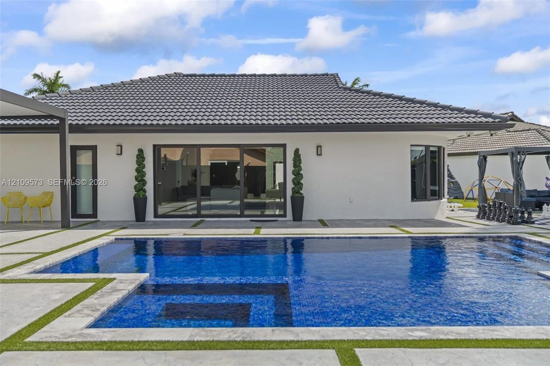 Stucco exterior with a tiled roof, featuring an in-ground swimming pool, stone-paver decking, and sliding glass panel doors