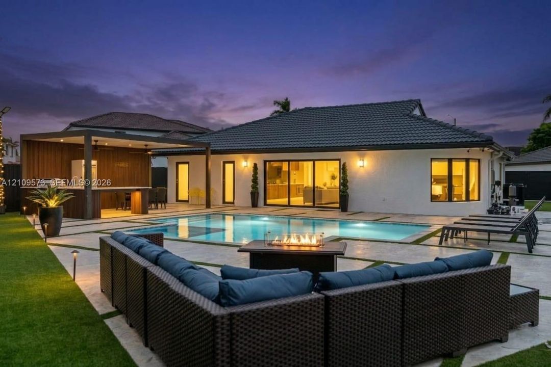 Outdoor living area featuring a covered kitchen structure, a built-in pool with spa, expansive stone patio with integrated turf strips, and sliding glass panel doors