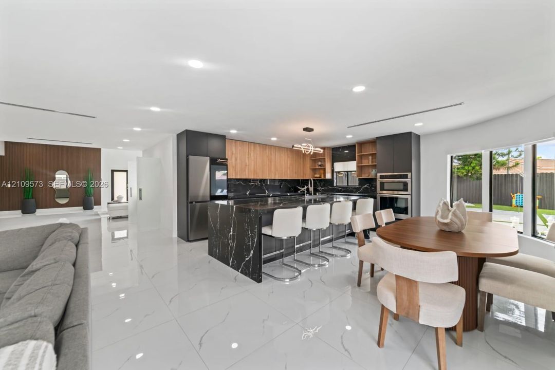 Kitchen featuring large center island with waterfall edge stone countertop, two-tone cabinetry, recessed lighting, and polished stone-finish flooring