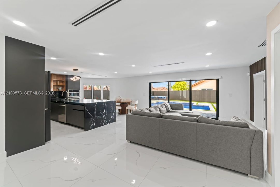 Open-concept interior featuring large-format tile flooring, recessed lighting, expansive multi-panel sliding glass doors, and a kitchen island with stone-finish waterfall countertop