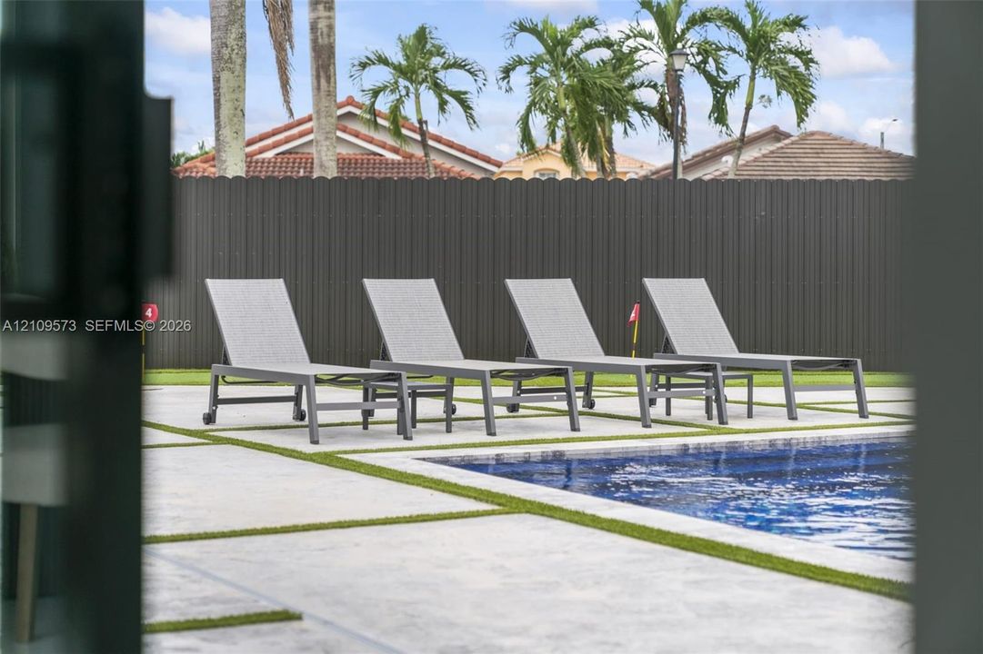 Outdoor swimming pool with a hardscaped patio featuring inlaid artificial turf joints and a privacy fence
