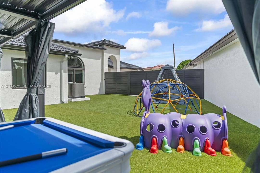 Rear exterior featuring a synthetic turf lawn, privacy fencing, and a covered patio area