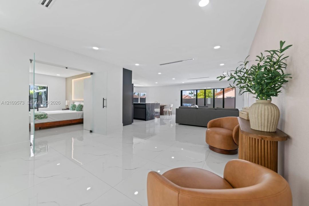 Open floor plan featuring large-format polished flooring, recessed lighting, floor-to-ceiling glass panel partitioning, and a kitchen island with dark stone-finish cabinetry
