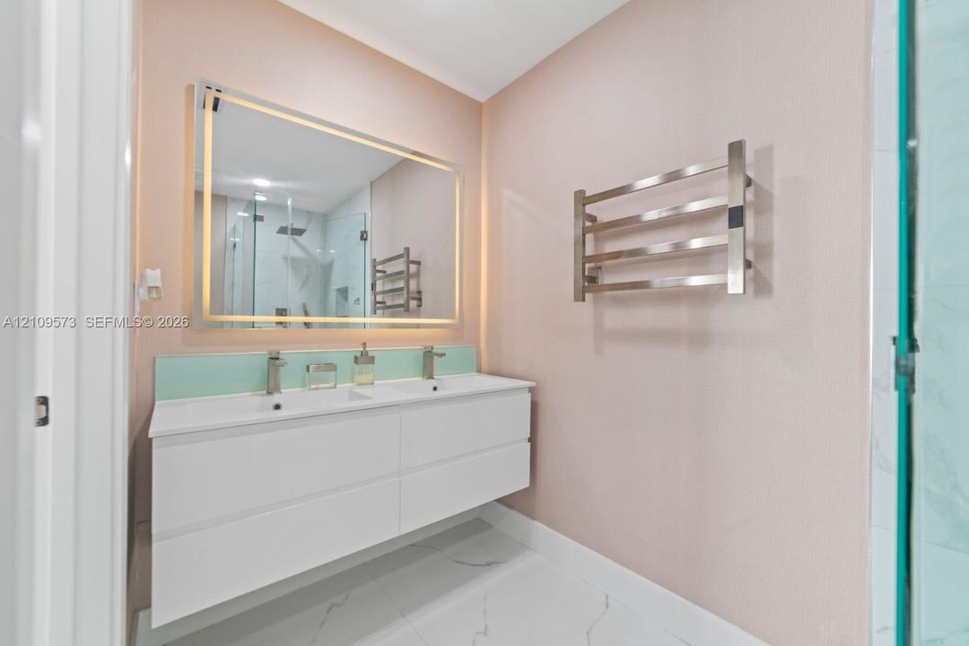 Floating dual-vanity with integrated sinks, back-lit mirror, wall-mounted heated towel rack, and large-format tile flooring