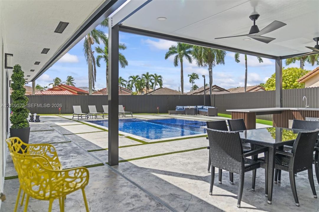 Covered outdoor patio featuring a concrete hardscape, built-in outdoor kitchen with sink, recessed lighting, ceiling fans, and an in-ground swimming pool
