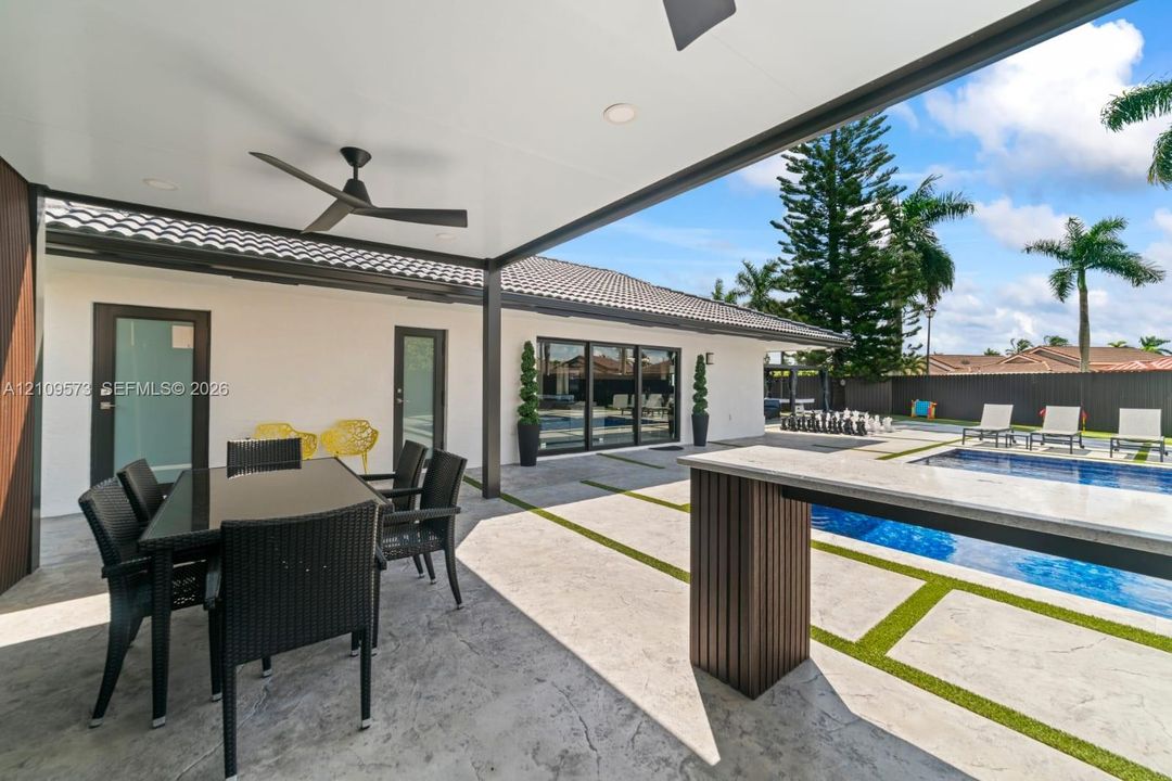 Covered patio featuring a recessed ceiling, stone-textured concrete flooring, a built-in outdoor bar with a stone countertop, a swimming pool, and turf-bordered hardscaping