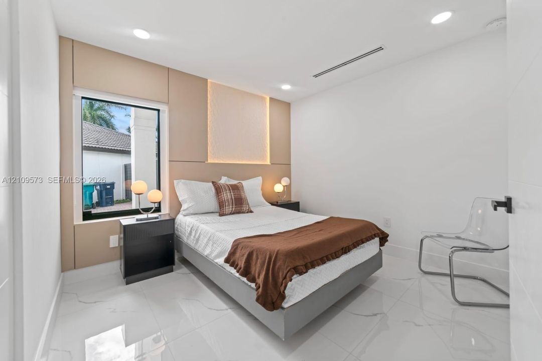 Neutral-toned accent wall with integrated LED backlighting, large-format tile flooring, recessed ceiling lighting, and black window framing