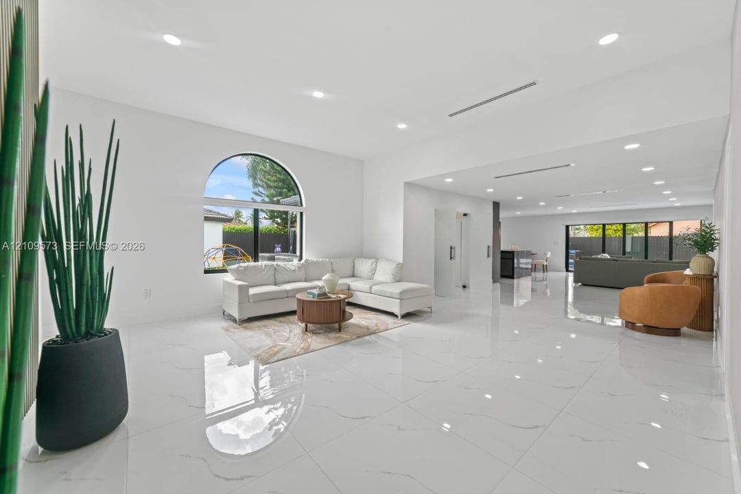 Large-format white polished tile flooring, arched window, recessed lighting, and expansive open interior layout