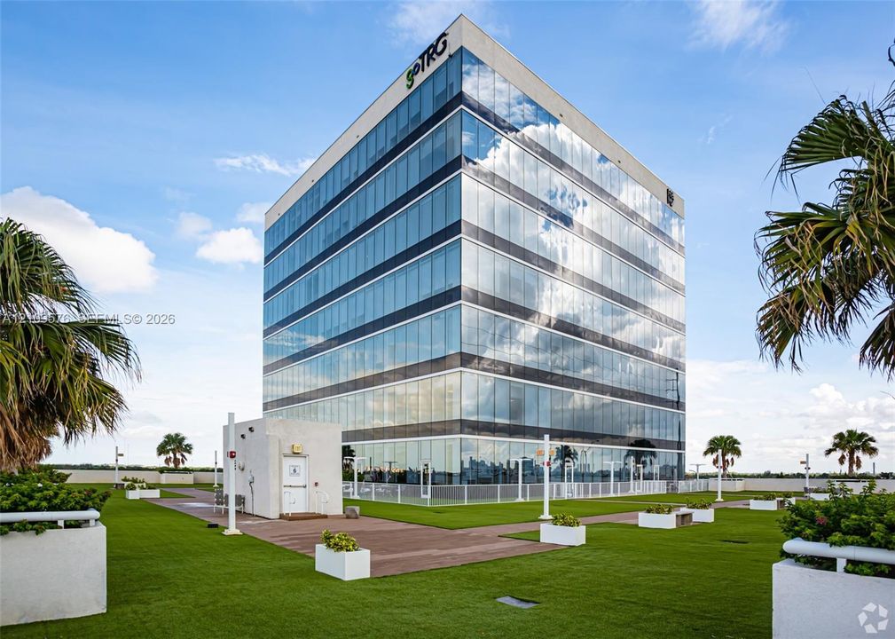 Multi-story glass-clad office building featuring a rooftop terrace, manicured green space, integrated planters, and hardscaped walkways