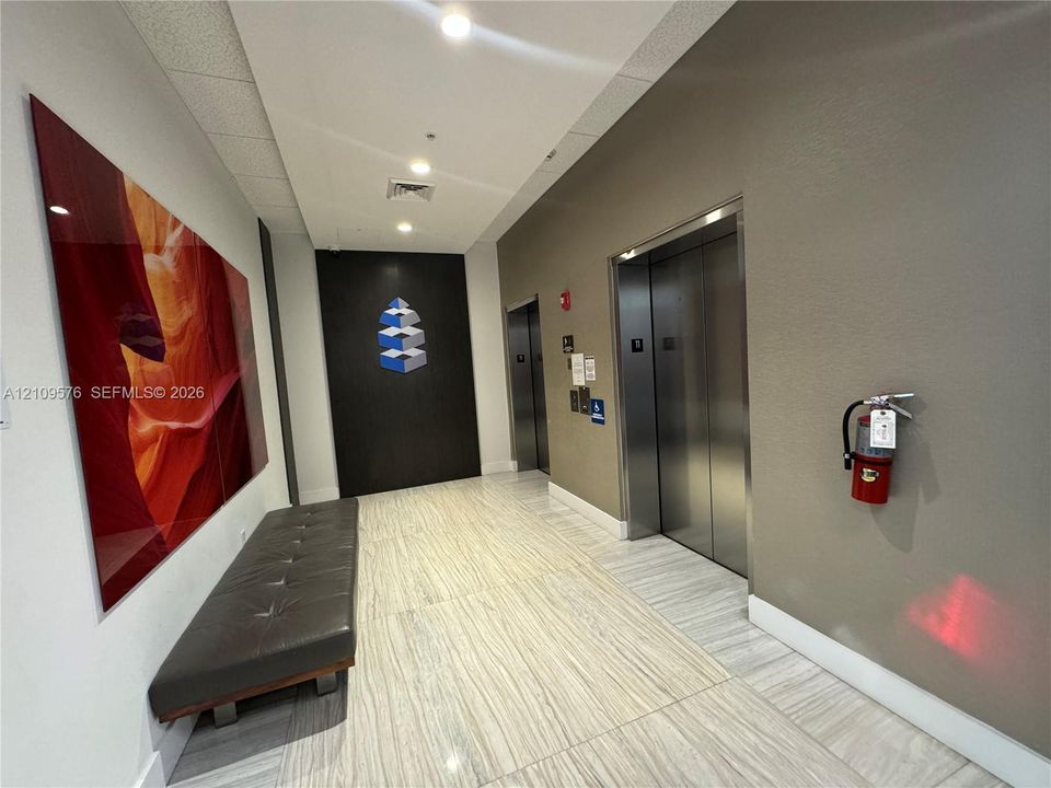 Common area featuring polished stone tile flooring, stainless steel elevator doors, recessed ceiling lighting, and a dark wood-finish accent wall