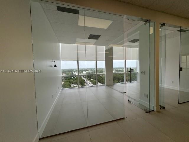 Floor-to-ceiling glass partitions, tile flooring, and expansive windows with roller shades