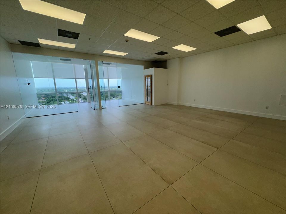 Open-concept interior featuring large-format tile flooring, recessed drop ceiling lighting, and floor-to-ceiling glass wall panels