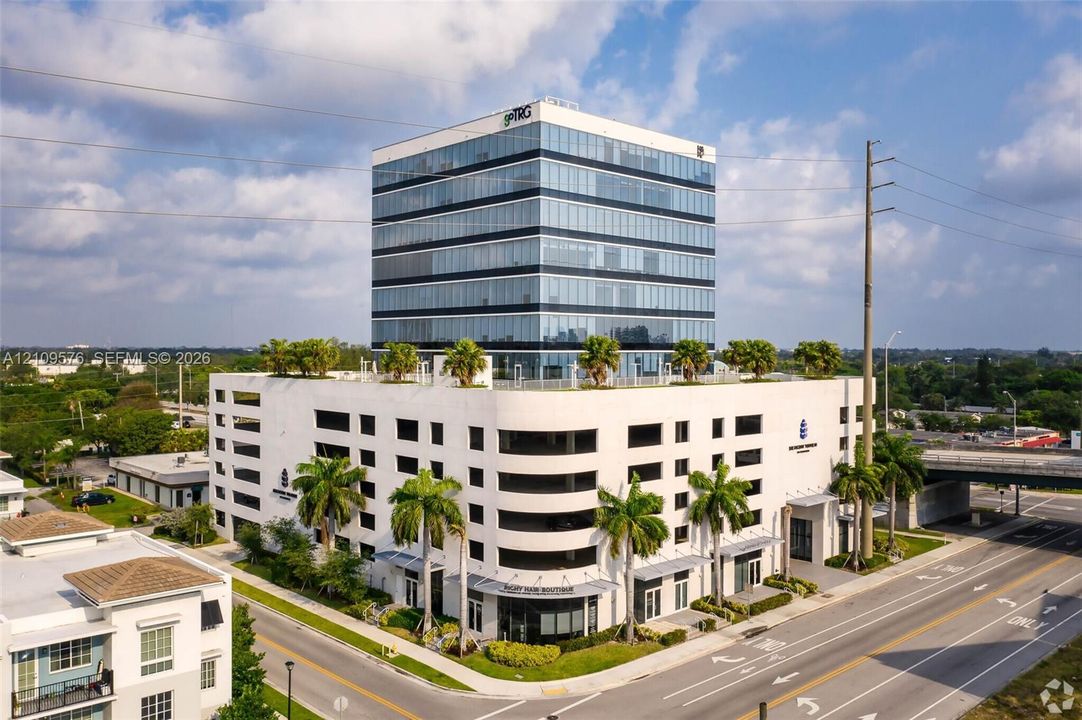Multi-story glass-facade professional building featuring a structured parking podium, rooftop landscaping, and ground-floor commercial entry points