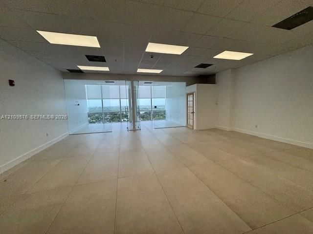 Large-format tile flooring, drop ceiling with recessed lighting, full-height glass partitions, and floor-to-ceiling windows with roller shades