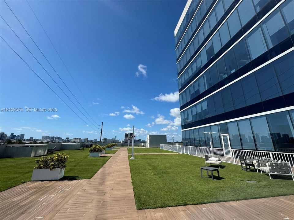 Rooftop terrace featuring synthetic lawn, wood-finish decking, integrated concrete planters, and metal perimeter railing