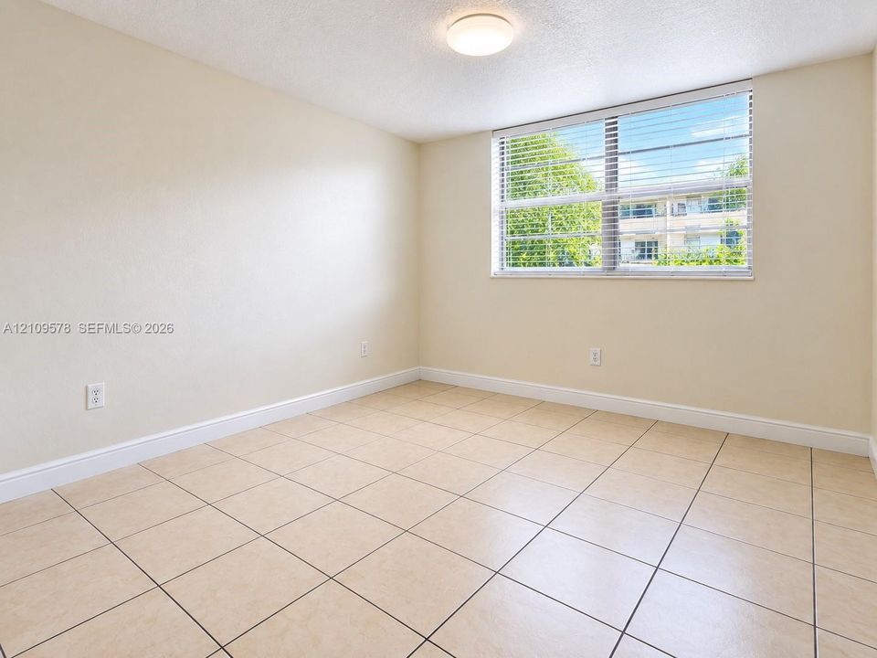 Neutral-toned room featuring large-format square tile flooring, a horizontal slider window with horizontal blinds, and a circular flush-mount ceiling light fixture