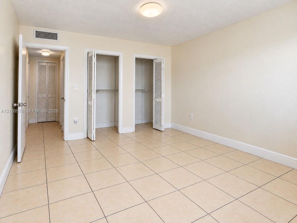 Neutral-toned tile flooring, two closets with louvered bi-fold doors, and a ceiling-mounted light fixture