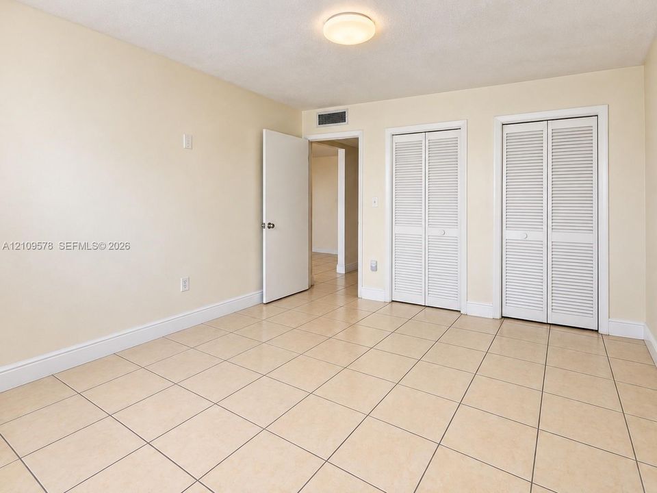 Neutral-toned tile flooring, two closets with white louvered doors, and a flush-mount ceiling light fixture