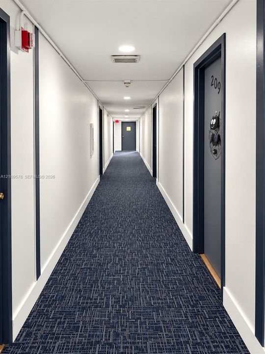 Hallway featuring neutral-toned walls, contrasting dark trim, patterned carpeting, recessed ceiling lighting, and uniform doors