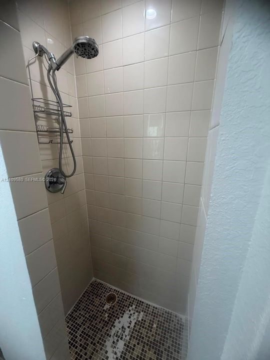 Shower stall featuring cream-colored wall tile, a multi-setting handheld shower head, polished chrome fixtures, and a mosaic-tiled floor