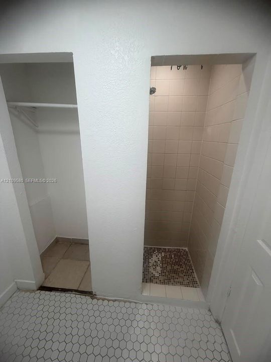 Recessed shower enclosure featuring ceramic wall tile, a decorative mosaic tile floor, and a built-in shower head, paired with a dedicated storage niche equipped with a hanging rod and ceramic floor tiling