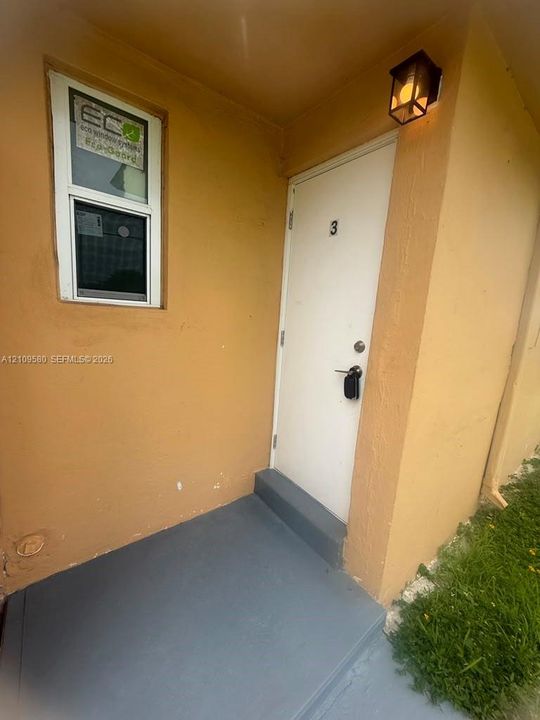 Entryway featuring a solid white door, rectangular window, painted concrete stoop, and an exterior wall-mounted light fixture
