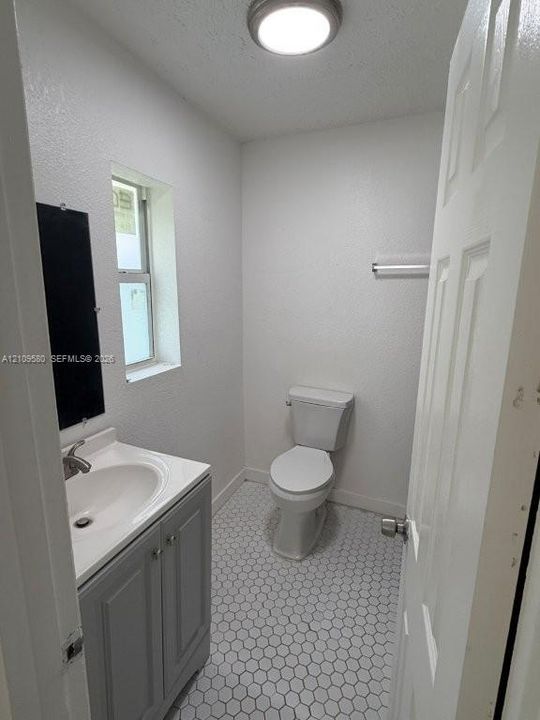 Vanity with a white integrated basin, grey shaker-style cabinet, hexagonal tile flooring, dual-flush toilet, and polished chrome hardware