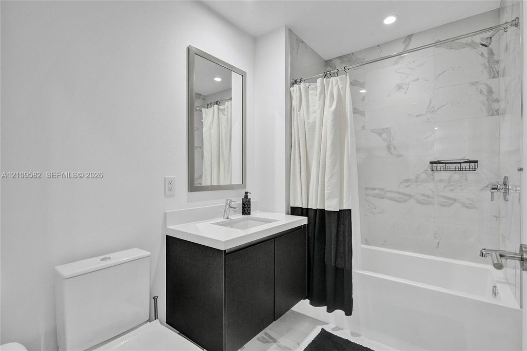 Floating vanity with a white countertop and rectangular basin, full-height wall tiling in the shower area, and recessed ceiling lighting