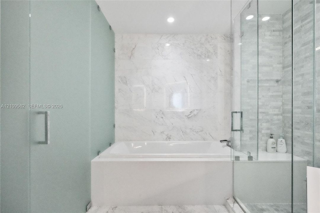 Soaking tub with stone-finish surround, glass-enclosed shower featuring tile walls, and recessed lighting
