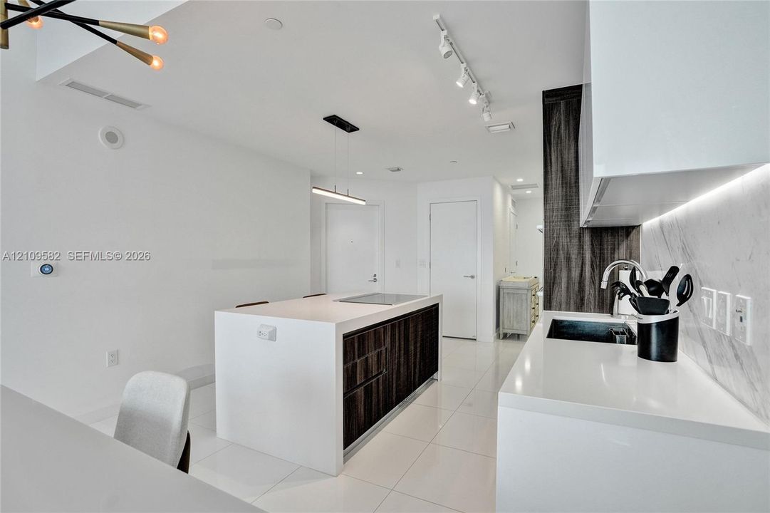 Kitchen featuring a waterfall-edge island with built-in cooktop, high-gloss white cabinetry, integrated under-cabinet lighting, tile backsplash, and polished flooring