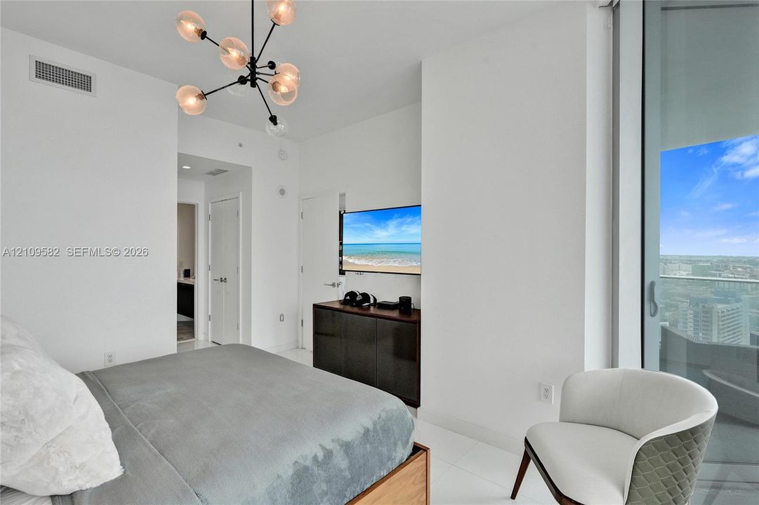 Modern bedroom featuring floor-to-ceiling glass sliding doors, polished tile flooring, a multi-arm sputnik chandelier, and neutral white wall finishes
