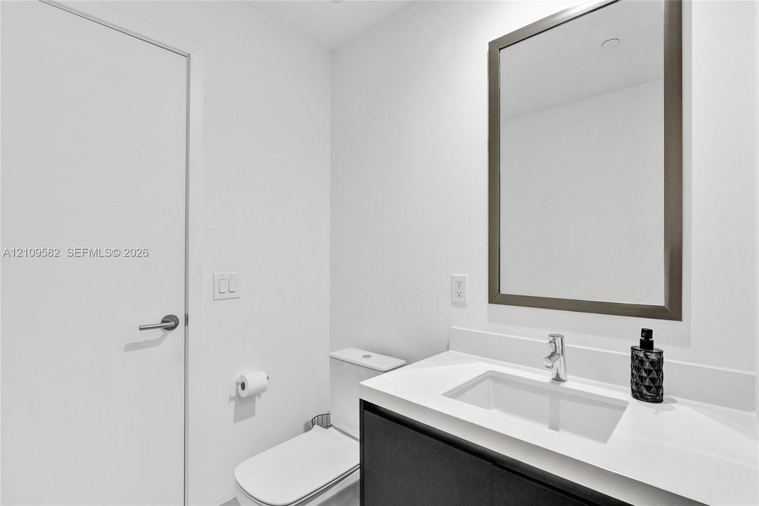 Modern vanity with a light-toned countertop, rectangular undermount sink, chrome faucet, and dark-finish base cabinetry, accompanied by a framed mirror