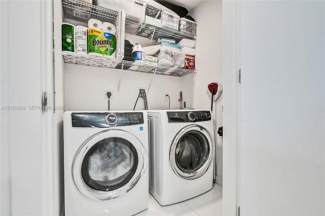 Laundry closet featuring a pair of white front-loading appliances and multi-level white wire shelving