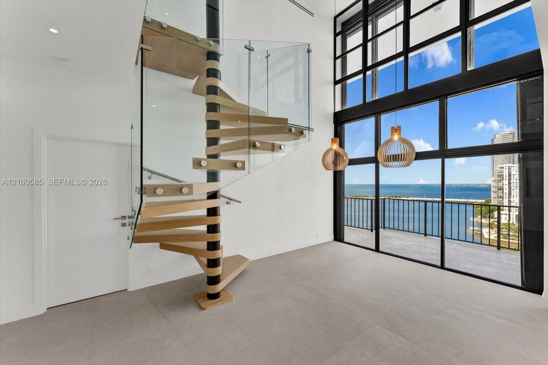 Architectural spiral staircase featuring wood-finish treads and a glass balustrade, floor-to-ceiling multi-panel windows, and pendant light fixtures