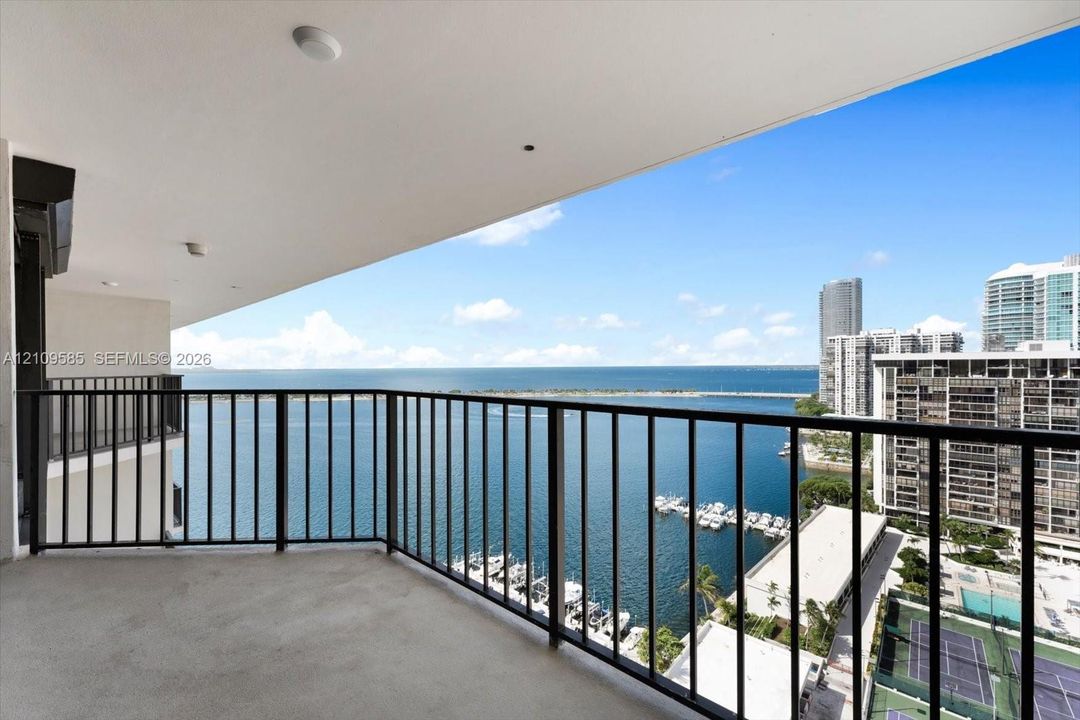 Covered balcony with black metal railing, concrete flooring, and water frontage