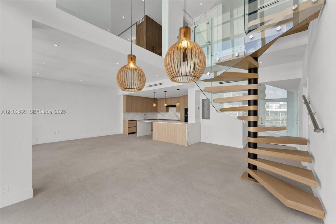 Spiral staircase featuring wooden treads and a glass railing, complemented by two large cage-style pendant lights, light wood-finish cabinetry, stone countertops, and tile flooring