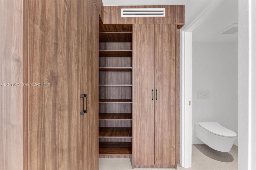 Floor-to-ceiling wood-finish cabinetry featuring open shelving, double-door storage, matte black hardware, and a wall-mounted toilet