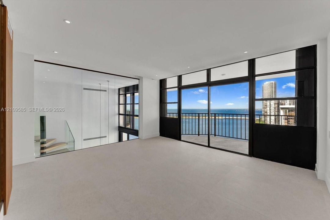 Primary Suite with exterior balcony, stone-finish flooring, glass-paneled interior partition, and staircase with glass railing